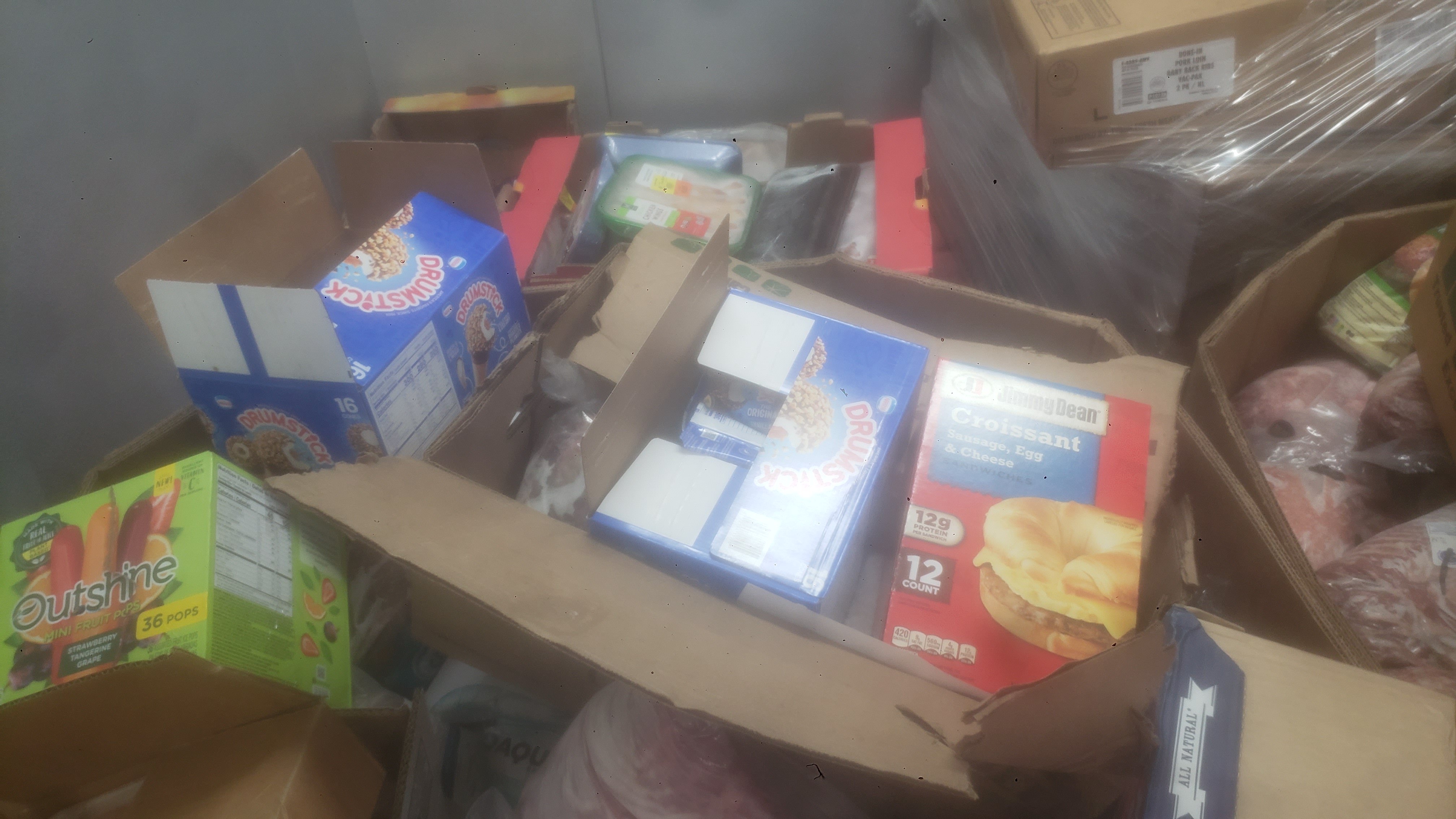 Assorted frozen items in cardboard boxes such as ice cream, meats, and breakfast sandwiches.
